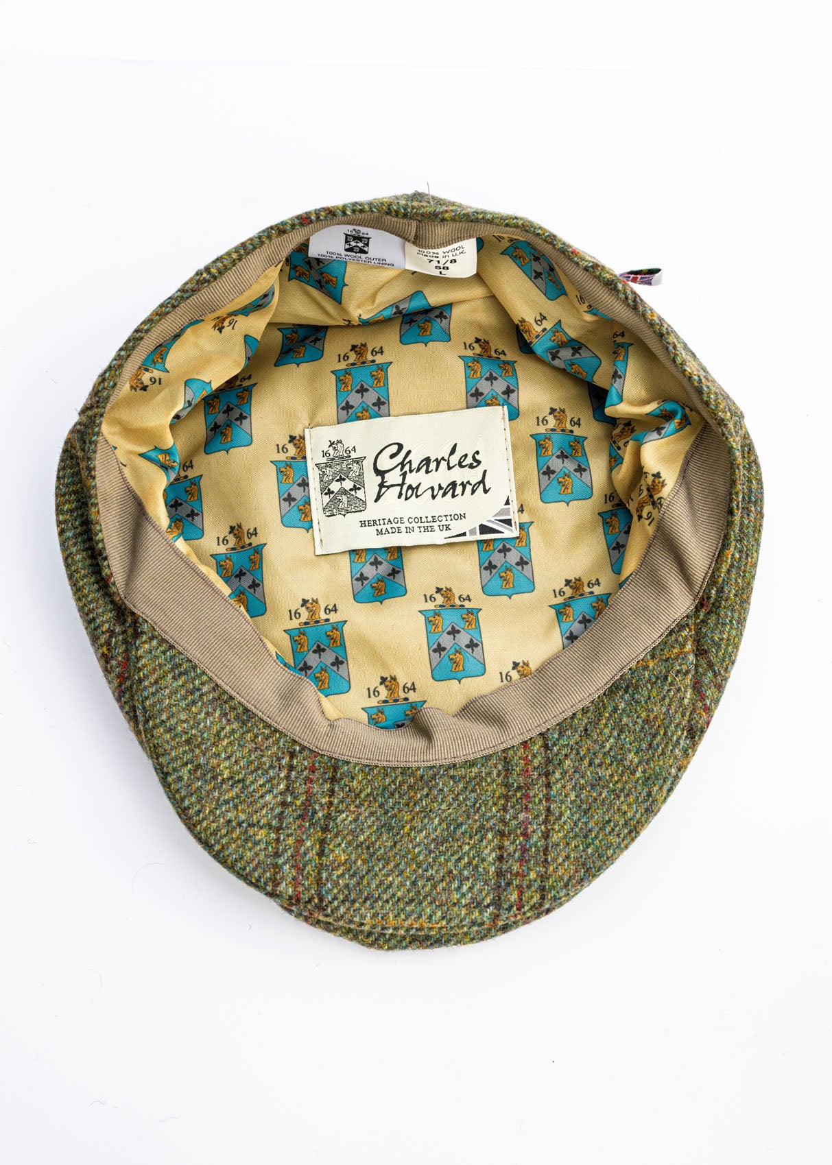 Green tweed flat cap with Yorkshire patterned interior and visible brand label on a white background
